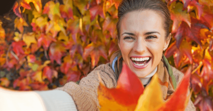 Smiling woman surrounded by autumn colored leaves.