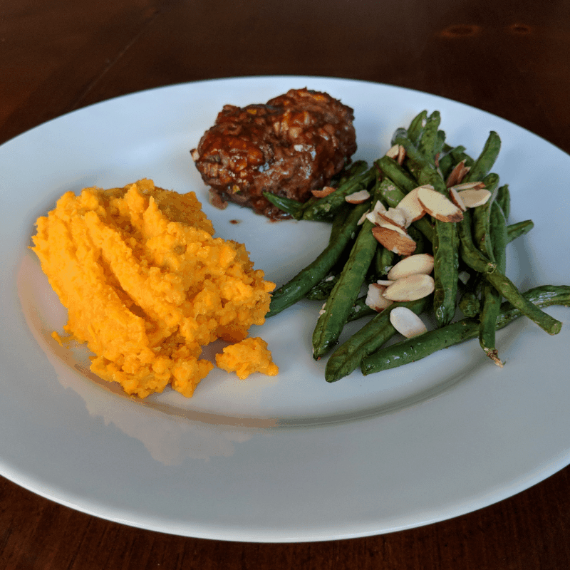 Sweet potatoes, green beans with sliced almonds, and mini meatloaf on white plate for high carb day dinner.
